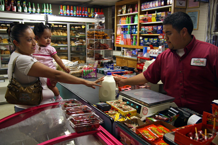 WIC_mother-shopping.jp: WIC participant Beatriz López holds her daughter, Blanca Arelí, while she shops for food at El Campesino Market in Richmond, CA July 20, 2011. Since 2009, almost half a dozen of small grocers in Richmond, like El Campesino, have become WIC certified. THE RATION/Felix Irmer